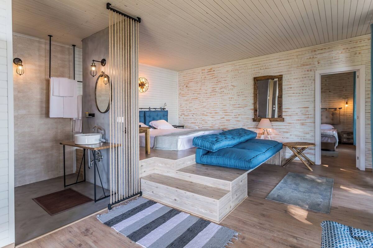 A modern bedroom with a large bed, a bedside table, a mirror, and a bathroom with a sink and towel rack.