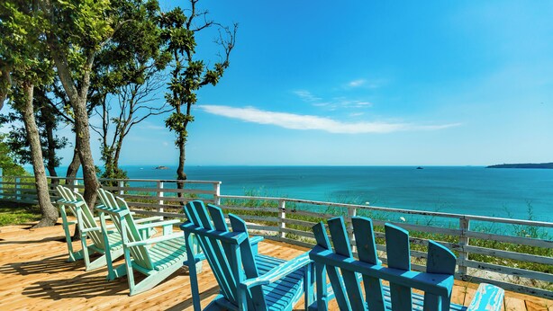 A wooden deck with blue Adirondack chairs overlooking a clear blue sea. - St. Anastasia Hotel (Burgas)