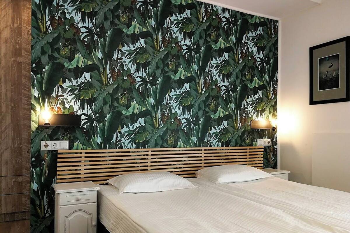 A bedroom with a bed, wooden headboard, nightstands, and a wall with a leafy wallpaper pattern.