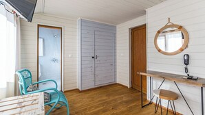 A room with a wooden floor, a teal chair, a wooden desk with a telephone, and a door leading to another room. - St. Anastasia Hotel (Burgas)