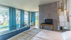 A modern bedroom with a large bed, a TV on a wooden stand, and a view of a lake through large windows. - St. Anastasia Hotel (Burgas)