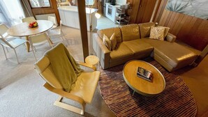 A modern living room with a sectional sofa, a round coffee table, and a dining area with a table and chairs. - Faraway-Chalet (Dinner Plain)
