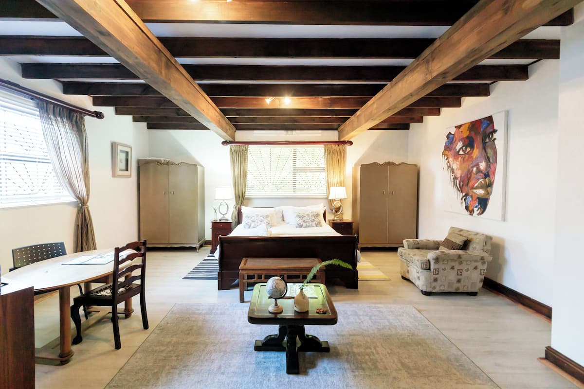 A bedroom with a large bed, a desk with a globe, a chair, a sofa, and a painting on the wall.