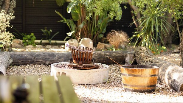 A rustic outdoor setting with a fire pit, a metal bucket, and logs. - Staymore Guesthouse (Stellenbosch)