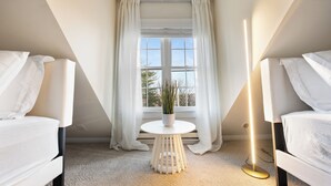 A modern bedroom with two white beds, a round white table with a potted plant, and a floor lamp. - Ultra-Modern Luxe Sleek & Stunning Stay (White Plains)
