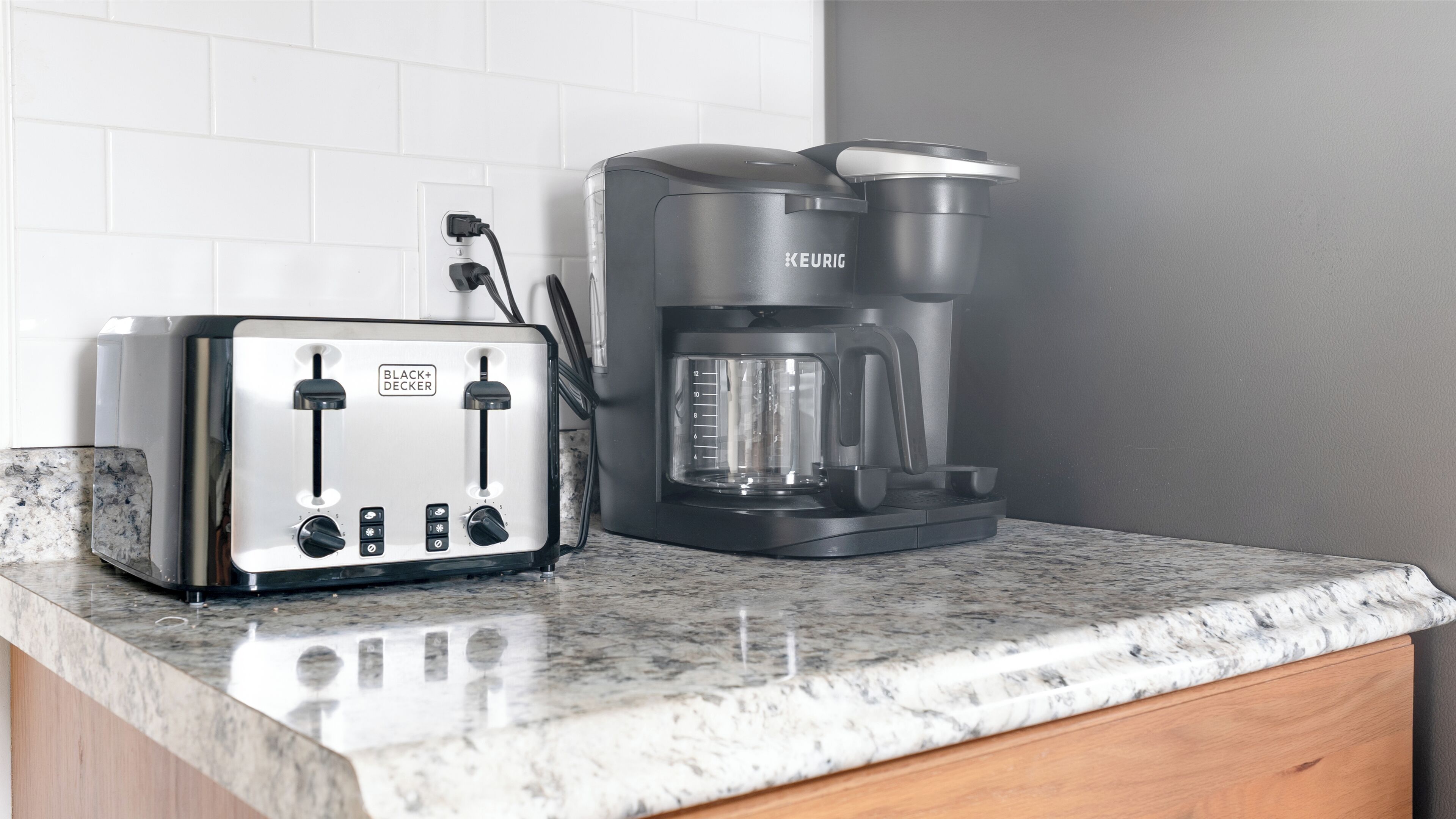 Una cocina con un tostador blanco y negro y una cafetera negra sobre una encimera de granito.