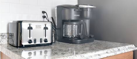 Una cocina con un tostador blanco y negro y una cafetera negra sobre una encimera de granito.