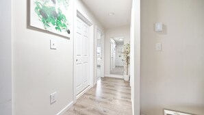 A hallway with white walls, a wooden floor, and a door at the end. - Ultra-Modern Luxe Sleek & Stunning Stay (White Plains)