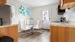 A modern kitchen with white cabinetry, a glass dining table, and a white door. - Ultra-Modern Luxe Sleek & Stunning Stay (White Plains)