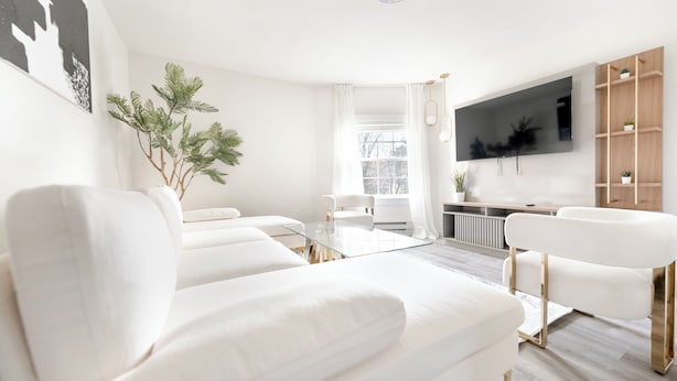 A modern living room with white sofas, a glass coffee table, a flat-screen TV, and a wooden TV stand. - Ultra-Modern Luxe Sleek & Stunning Stay (White Plains)