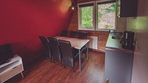 A compact kitchen with a dining area, wooden ceiling beams, and a window with a view of greenery.