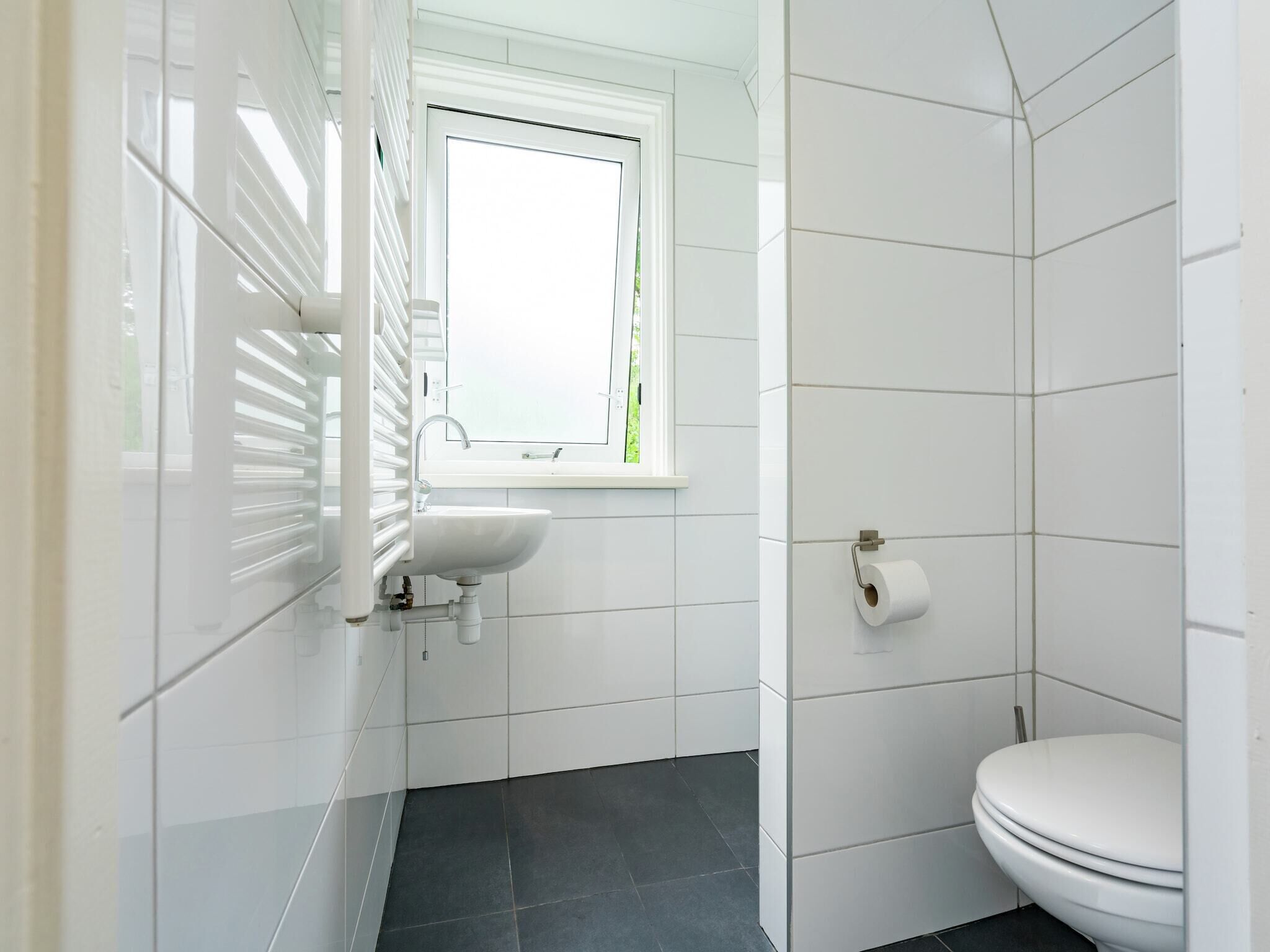 A bathroom with white tiles, a sink, a toilet, and a window.