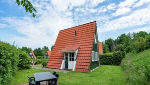 A house with a sloped red roof, a green door, and a brick patio with a table and chairs.