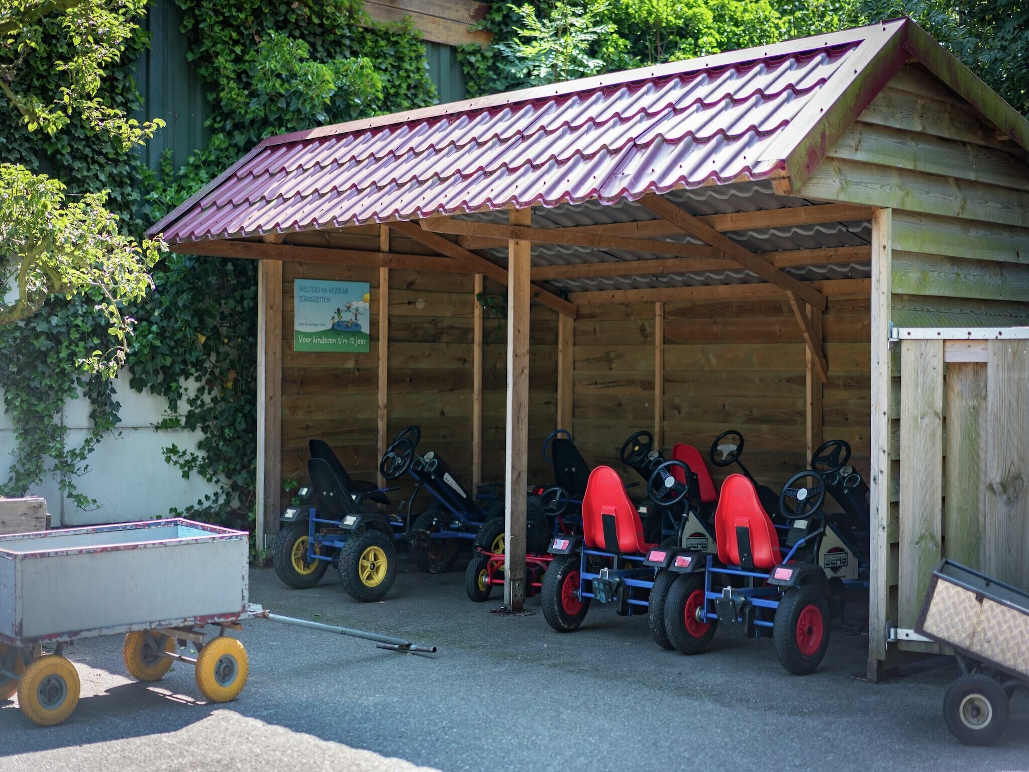 Une structure en bois surmontée d’un toit en métal ondulé, qui pourrait être un abri de voiture ou un garage, et à l’intérieur duquel sont garés plusieurs petits véhicules.
