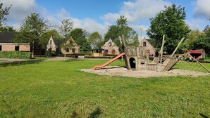 A playground with a slide and climbing structures, surrounded by green grass and trees.