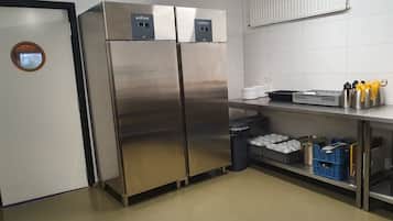 Een keuken met roestvrijstalen apparatuur, een prullenbak en opbergplanken.