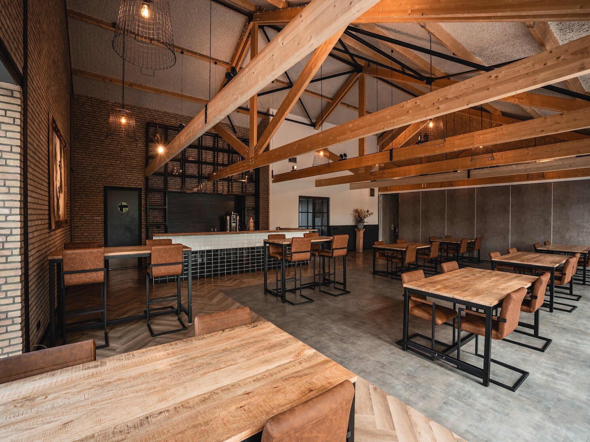 A spacious restaurant with high ceilings and exposed wooden beams, featuring a mix of bar seating and individual tables.