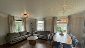 A spacious living room with a large round table, sofas, and a floor lamp. - Large Countryside Group Stay (Bant)