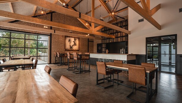 A spacious dining area with high ceilings, exposed beams, and large windows offering views of the outdoors. - Large Countryside Group Stay (Bant)