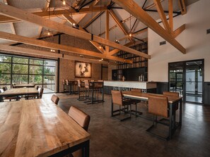 A spacious dining area with high ceilings, exposed beams, and large windows offering views of the outdoors. - Large Countryside Group Stay (Bant)