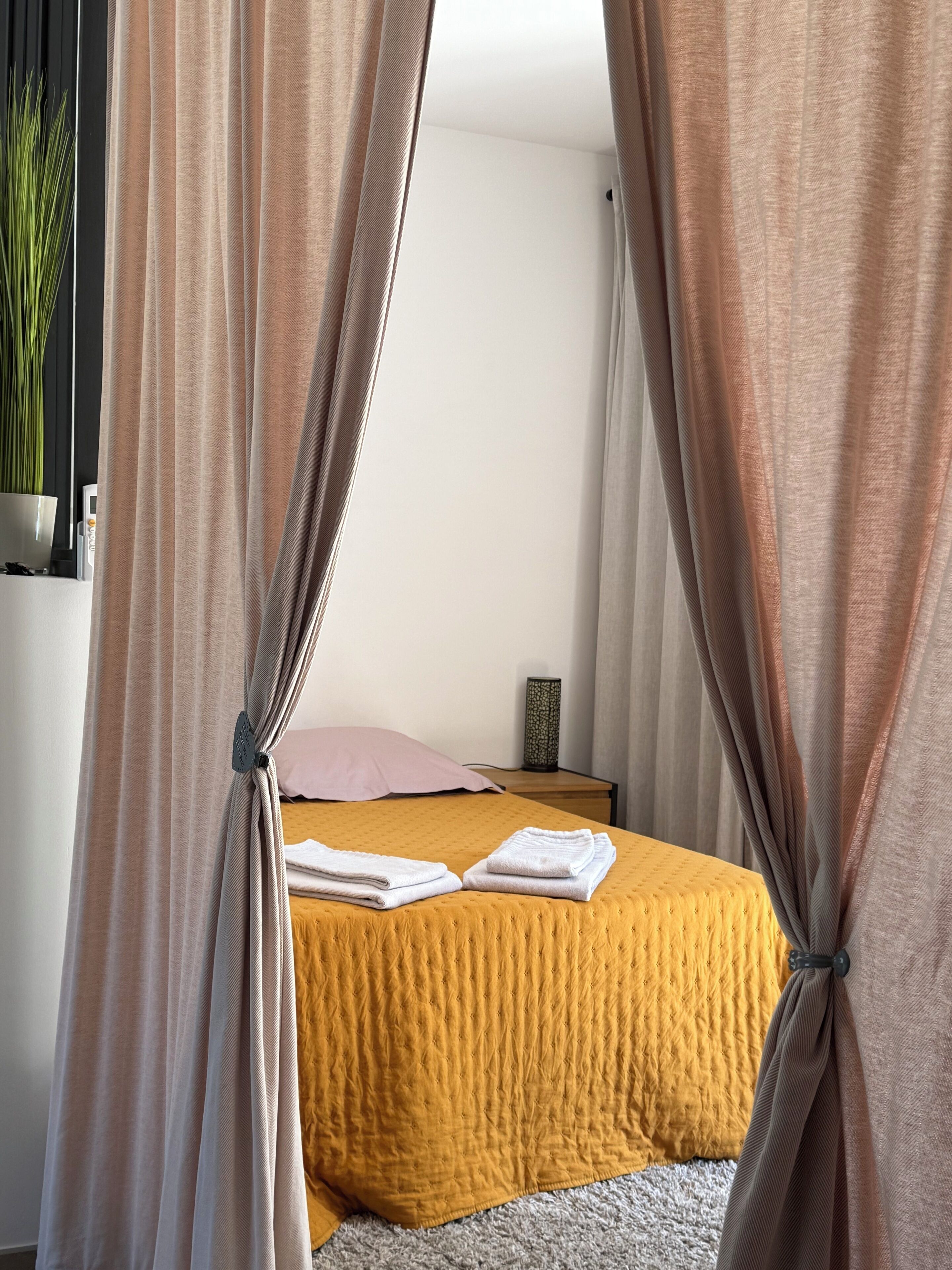 A neatly made bed with a yellow quilt, a bedside lamp, and a pink pillow.