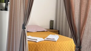 Een keurig opgemaakt bed met een gele sprei, een bedlampje en een roze kussen.