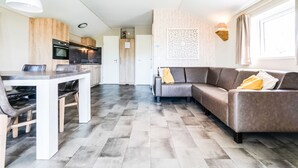 A modern living room with a sofa, a dining table with chairs, and a kitchen area with cabinets and appliances.