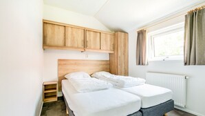 A bedroom with two beds, wooden cabinets, a window with curtains, and a radiator.
