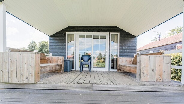 A covered deck with a wooden floor, a chair, and a trash bin.