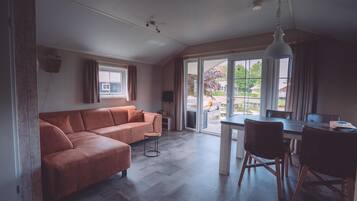 Un salon moderne avec un canapé d’angle, une table à manger avec des chaises et une grande porte-fenêtre coulissante donnant sur un balcon.