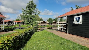 A row of wooden cabins with red roofs, a grassy area, and a pond. - Pondside Stay w/ Kitchen (Bant)
