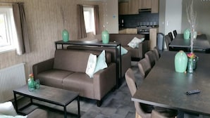 A modern living room with a sofa, coffee table, and dining table. There is a kitchen area in the background. - Pondside Stay w/ Kitchen (Bant)