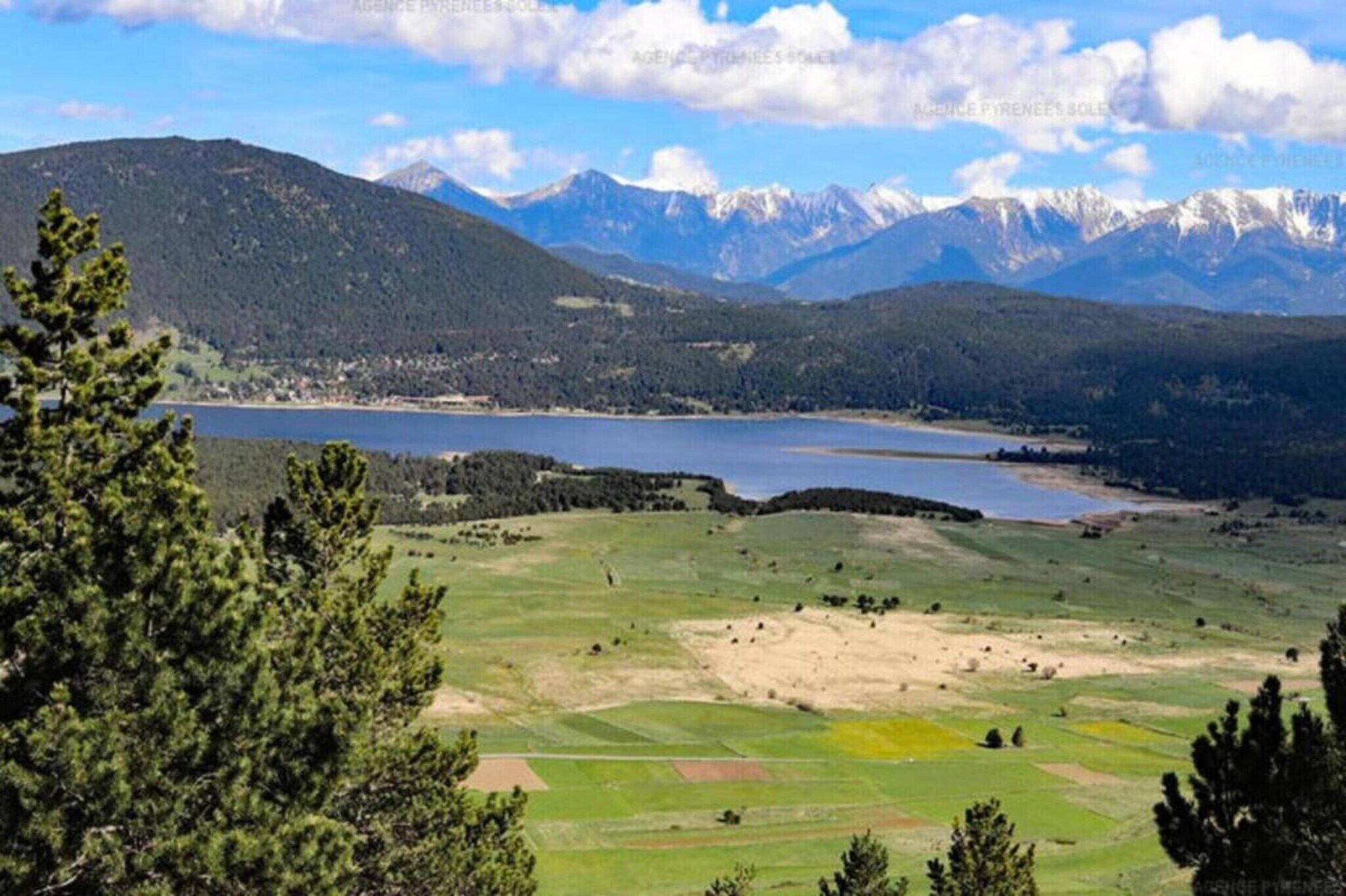 Un paysage montagneux avec un lac, des zones boisées et un ciel dégagé.