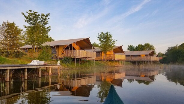 A lakeside accommodation with wooden cabins, a dock, and a calm water body reflecting the structures.