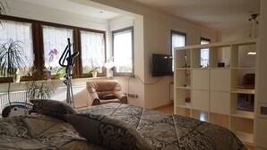 A bedroom with a large bed, a chair, a TV, and built-in shelving.