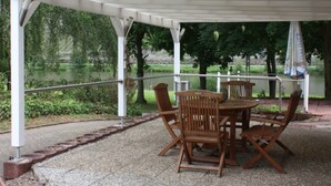 A covered patio with wooden furniture and a view of a lake.