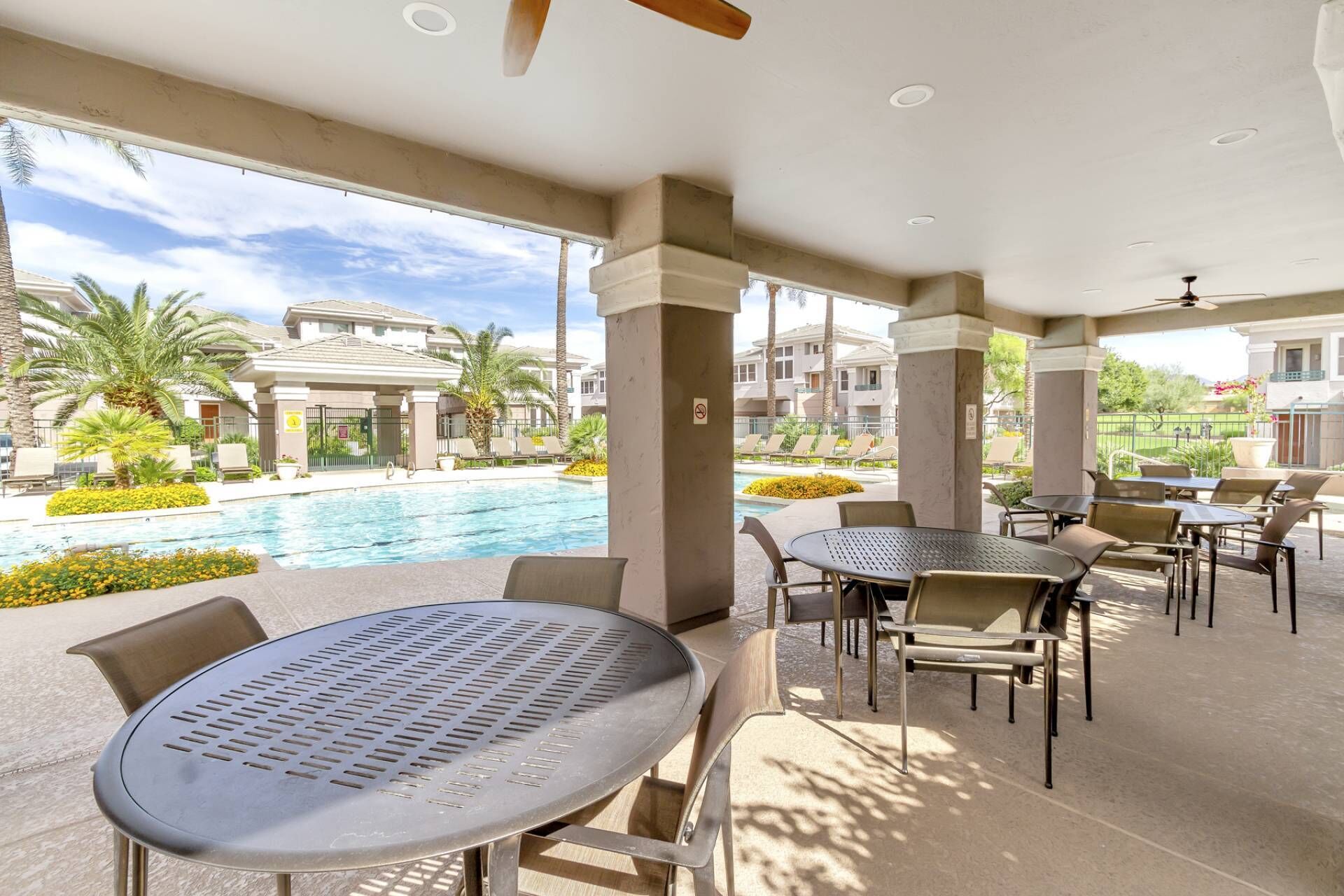 A poolside area with tables and chairs, a pool, and a view of the resort buildings.