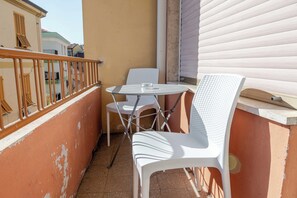 A balcony with white plastic chairs and a table, a railing, and a view of neighboring buildings.