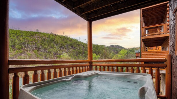 A hot tub on a wooden deck with a view of a forested hillside. - Sleeps 28 | Indoor Pool, Theater, Game Room, Hot Tub, Views | Marco Polo Lodge (Sevierville)