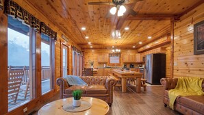 A wooden cabin interior with a dining area, kitchen, and seating. - Sleeps 28 | Indoor Pool, Theater, Game Room, Hot Tub, Views | Marco Polo Lodge (Sevierville)