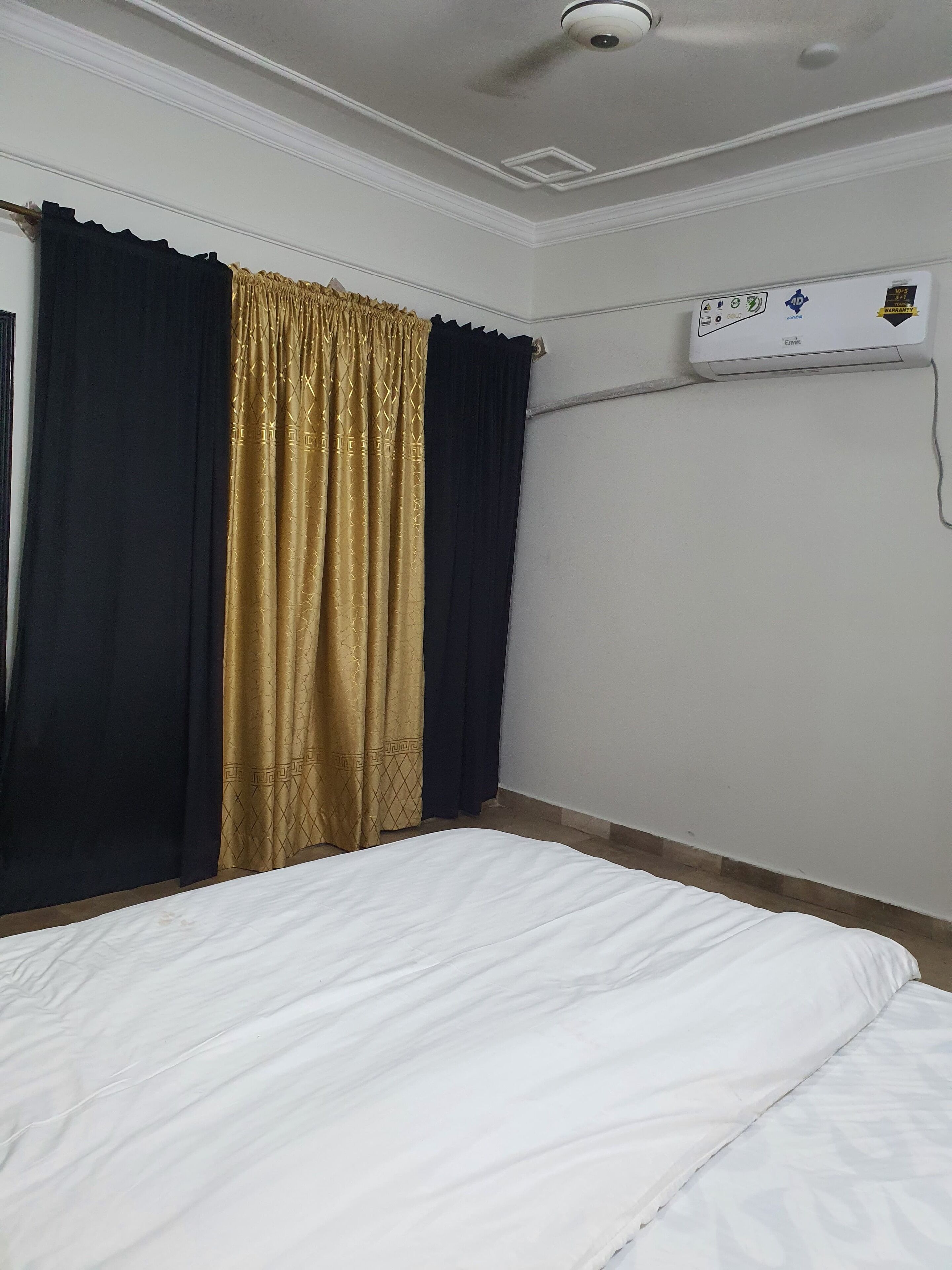 Ein Hotelzimmer mit Bett, dunklen Vorhängen, Deckenventilator und Klimaanlage.
