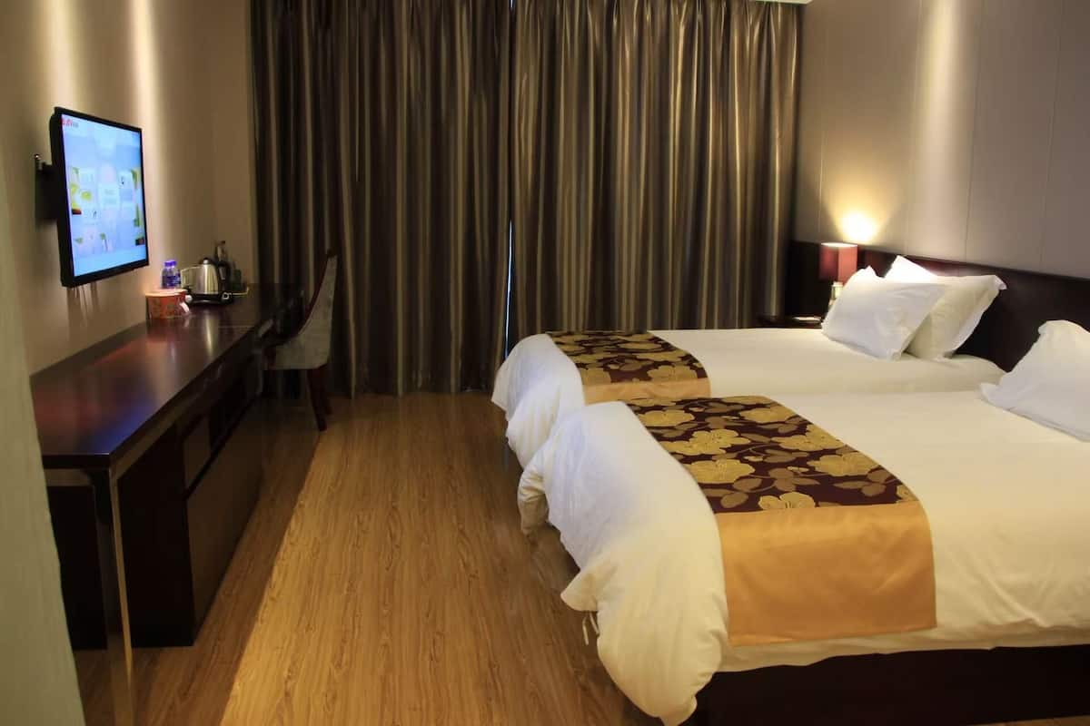 Een hotelkamer met een bed, een bureau, een stoel, een televisie en gordijnen.