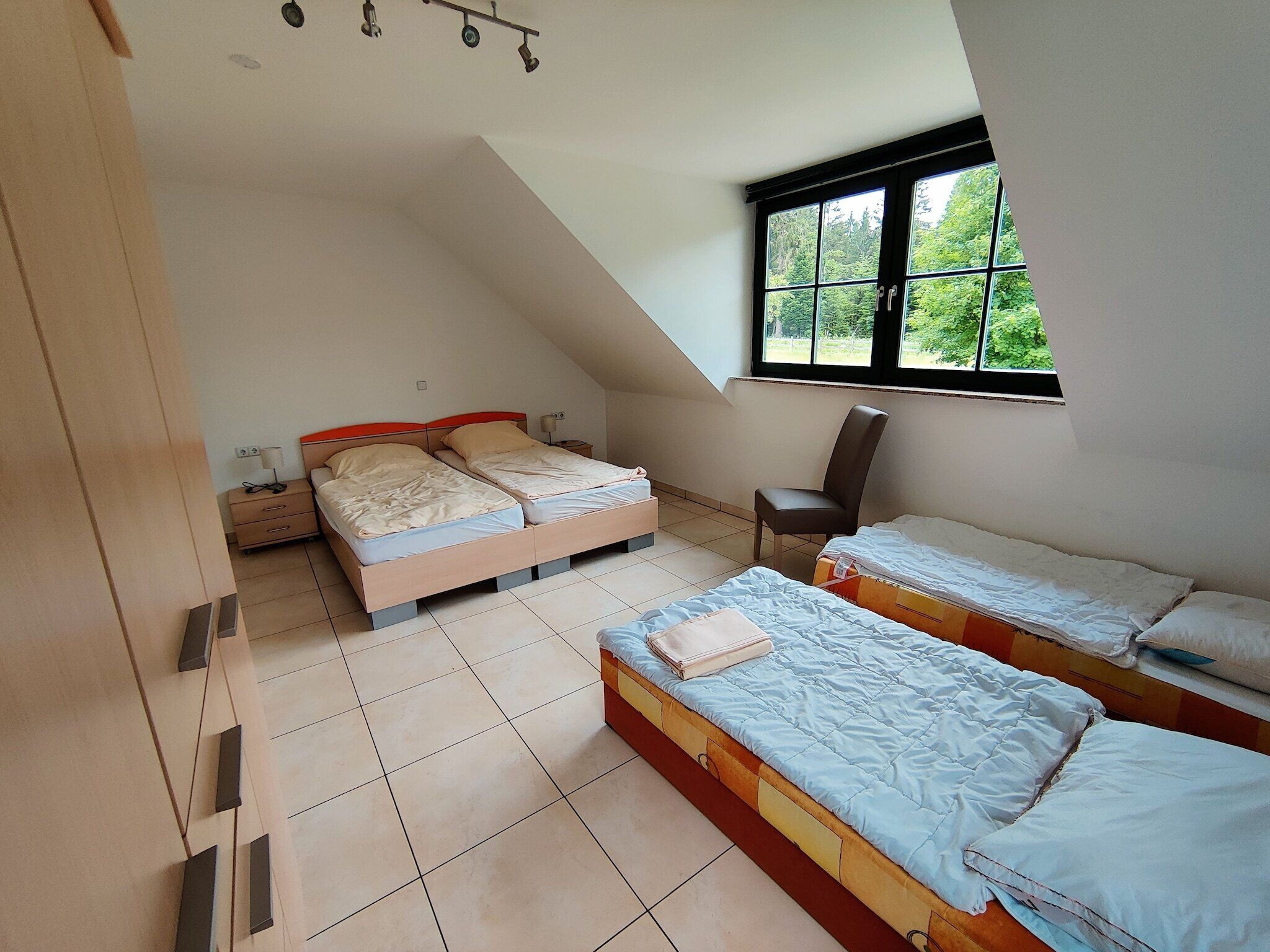 A bedroom with two beds, a chair, and a window with a view of trees.