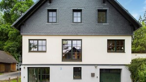 A two-story house with a steeply pitched roof, multiple windows, and a garage door. - Pet-Friendly Getaway (Eisfeld)