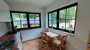 A small kitchen with a dining area, two windows with black frames, a tiled floor, and a view of greenery outside. - Pet-Friendly Getaway (Eisfeld)
