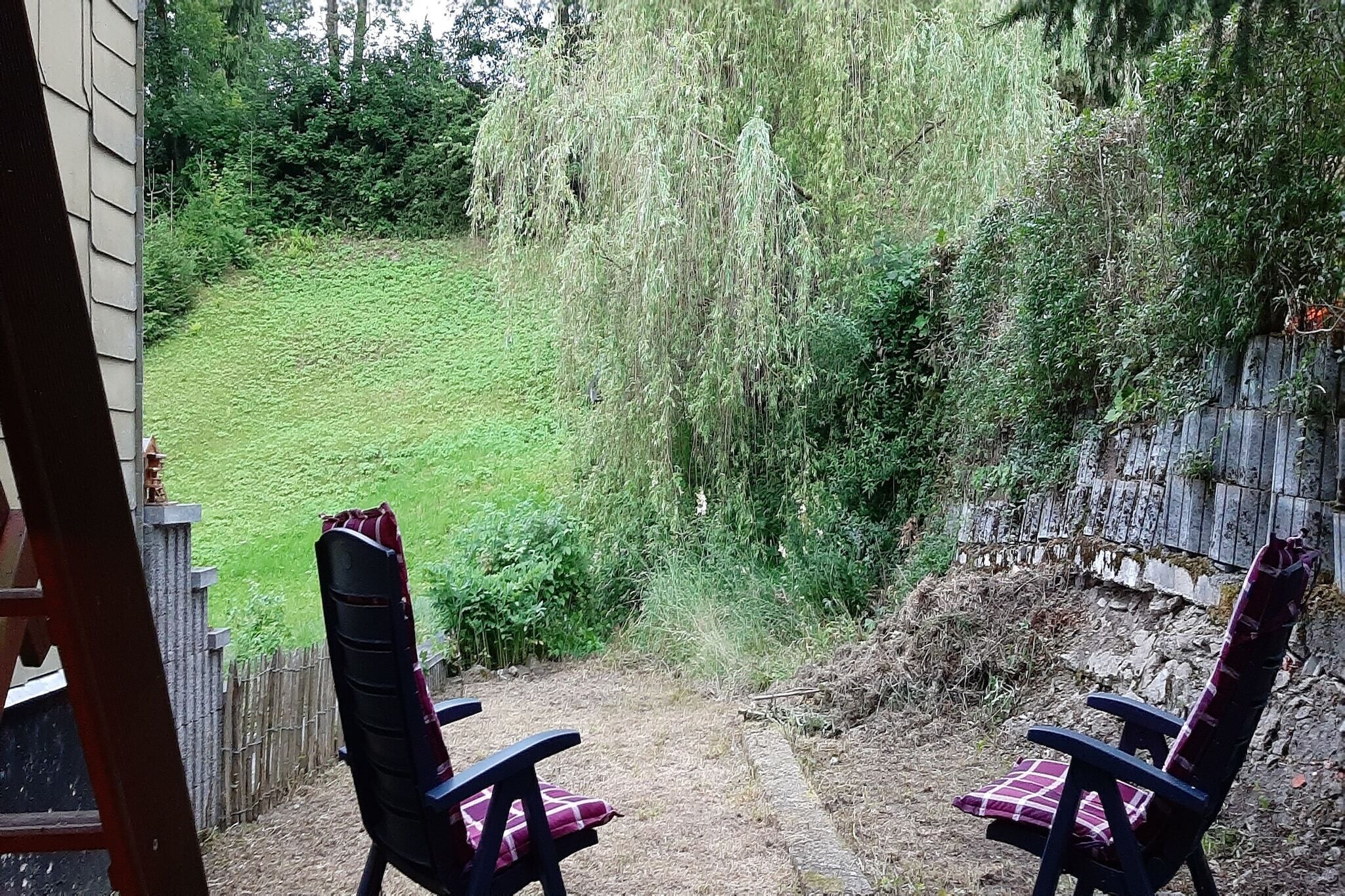 Eine Terrasse mit zwei Stühlen und Blick auf eine Rasenfläche mit einer Trauerweide.
