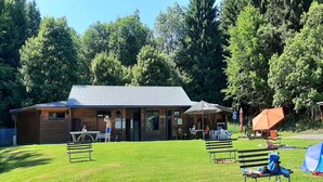 A building with a tiled roof, a brick facade, and a grassy area with benches and a tent. - Cosy holiday home near the ski lift (Altenfeld)