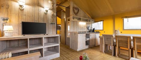 A rustic cabin interior with a wooden TV stand, a dining area with benches, and a kitchen area with a sink and cabinets.