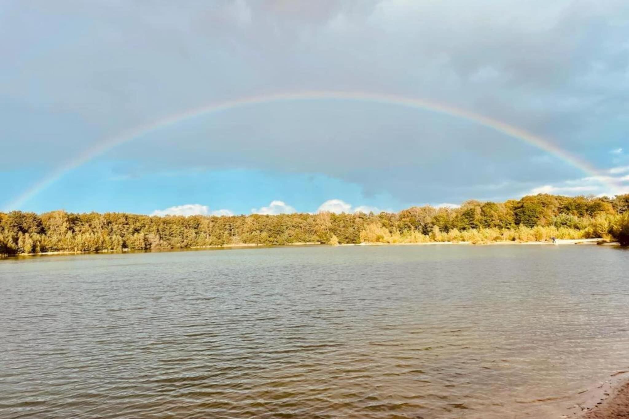 Ein See mit einem Regenbogen über einem bewaldeten Gebiet.