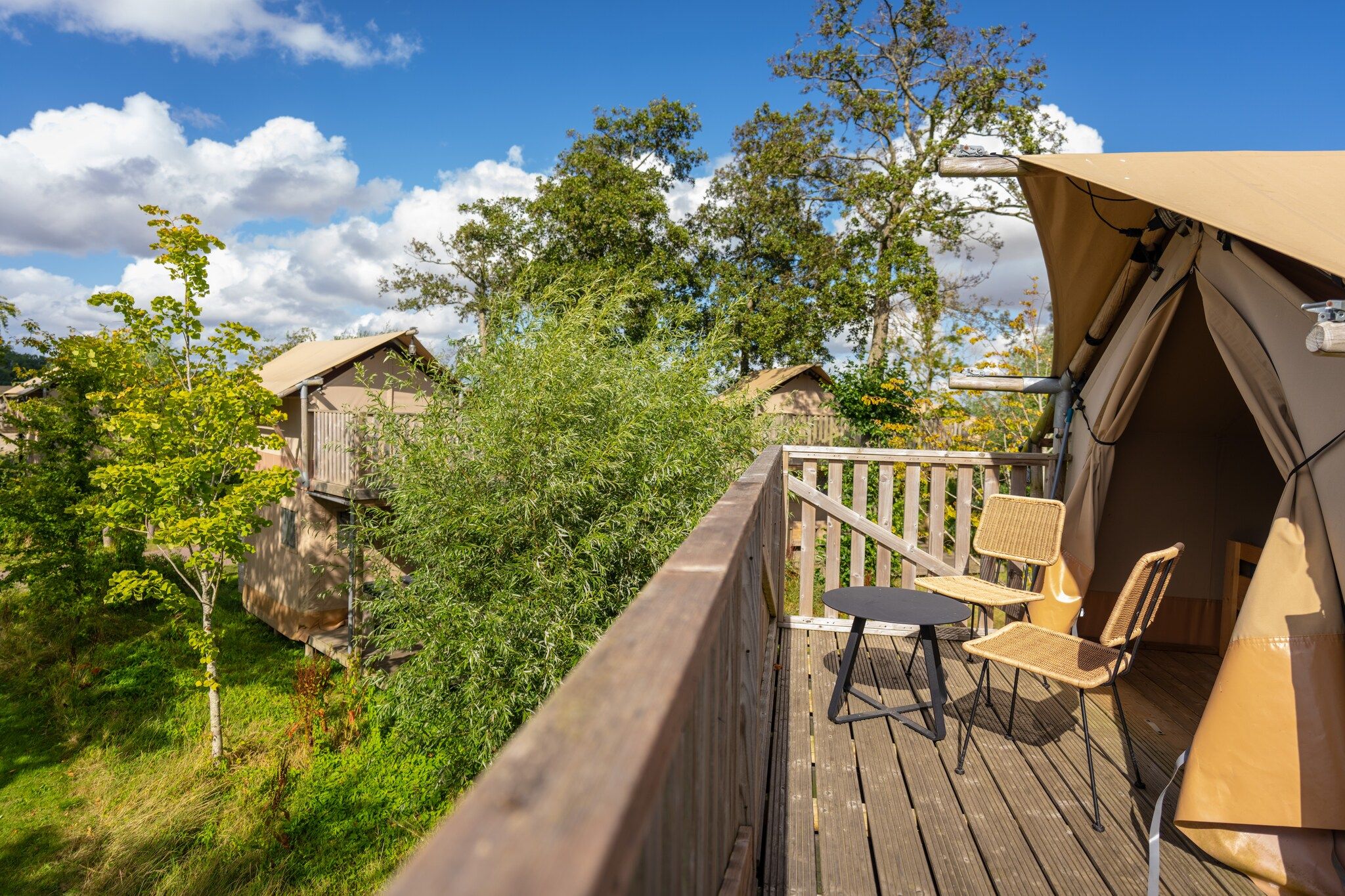 A wooden deck with outdoor furniture, a covered area with a table and chairs, and surrounding greenery.